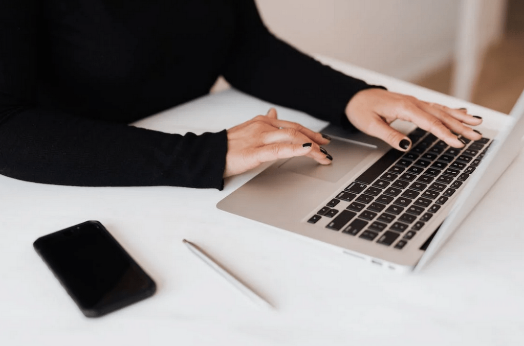 Kvinnas händer på en laptop vid ett vitt skrivbord